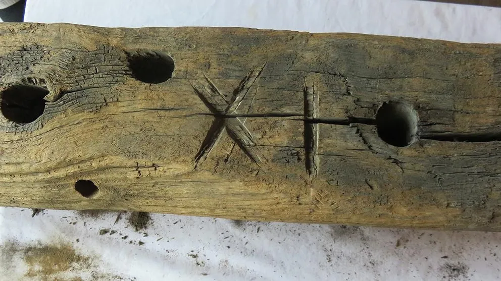 A close up of a piece of wood with holes drilled and the numbers XI roughly carved into its surface