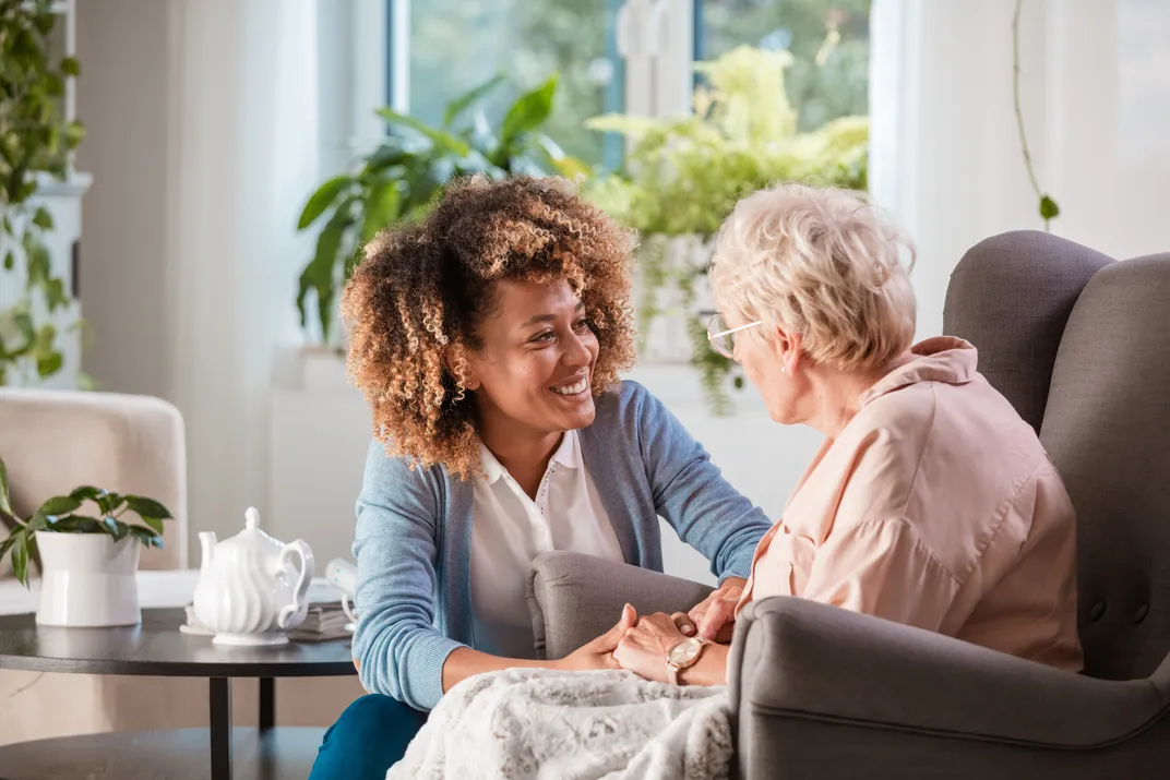 a nurse talks to an elderly woman sitting in a chair