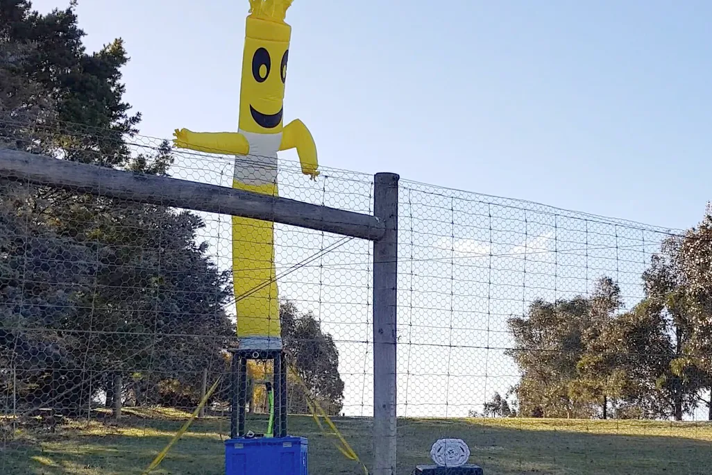 An inflatable yellow tube man stands behind a fence.