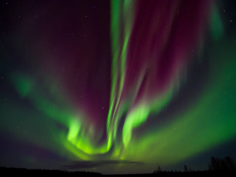 Green and purple northern lights color the night sky above a mountain range
