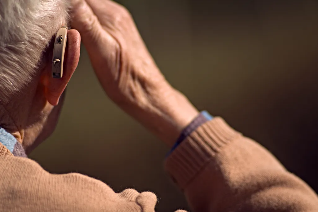 A person wearing a hearing aid, seen from the back, touches their head