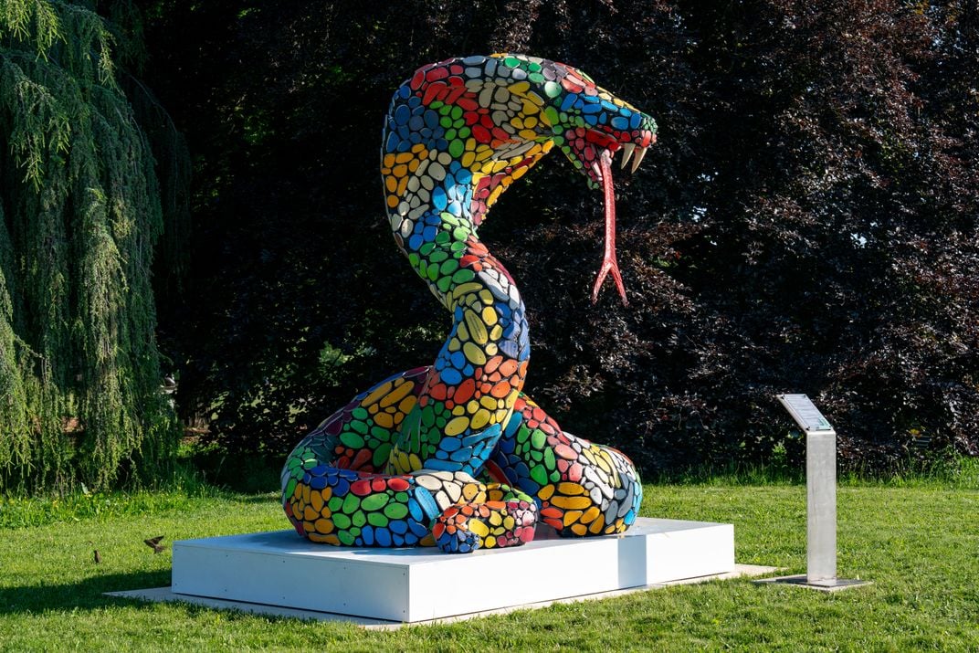 Large colorful snake sculpture on pedestal on grass