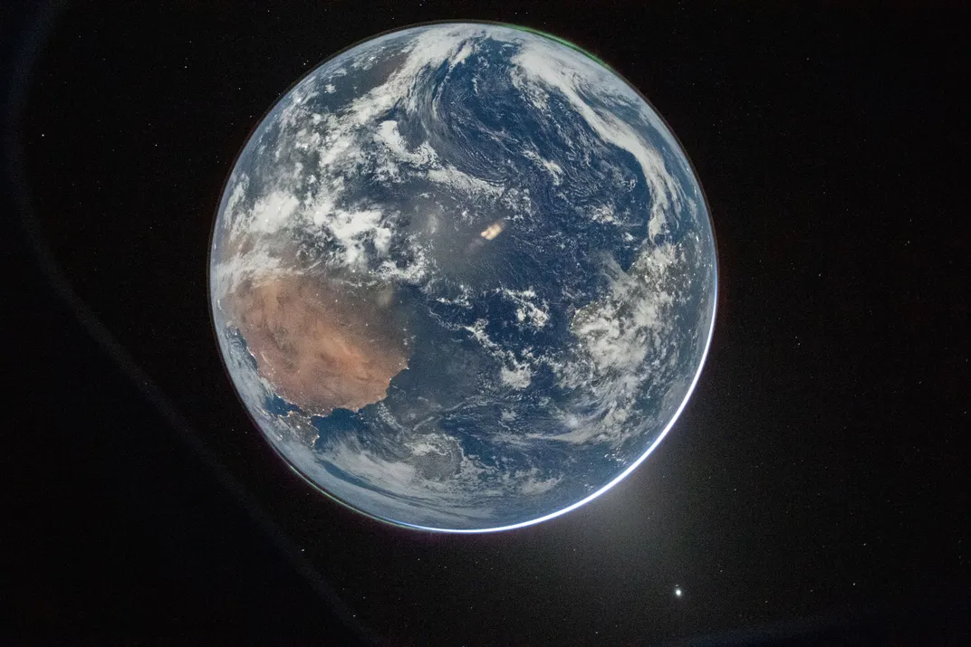 Earth from space, a glow of white light at the lower right and faint green glows at the upper right and lower left