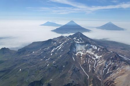 An aerial oblique photo of the volcanoes of the Islands of Four Mountains in Alaska's Aleutian Island chain. In the center is the summit of Mount Tana. Behind Tana are (left to right) Herbert, Cleveland and Carlisle Volcanoes.
