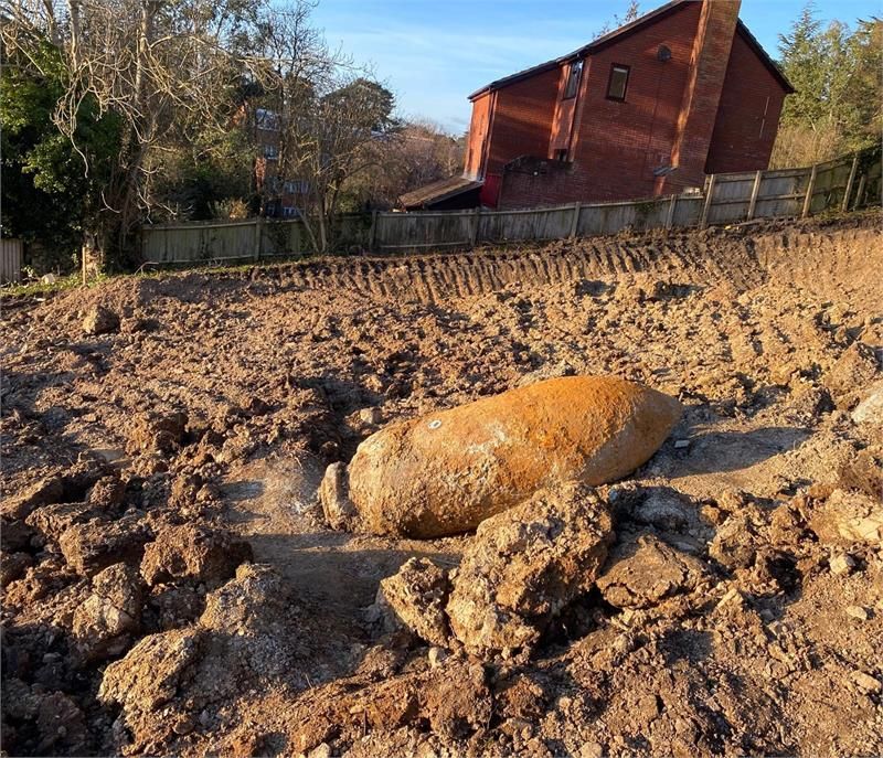 A muddy field with a red barn and house in the background, with a large orange piece of metal sitting in the middle of the field