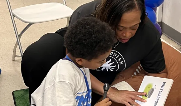 A woman reads with a young boy, the book says "wheelbarrow" in big letters