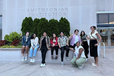 A group of student interns gather in front of a grey building