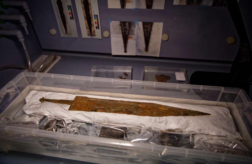 An old sword laid out flat in a plastic box