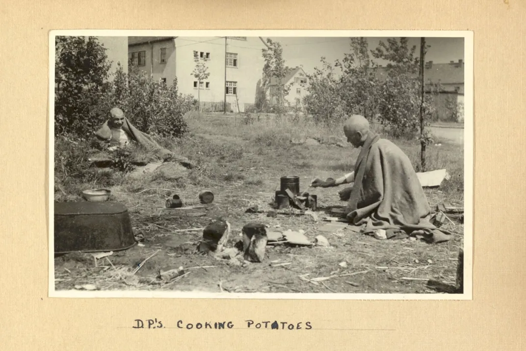 A photograph of Bergen-Belsen survivors cooking potatoes over a stove in the ruins of the concentration camp
