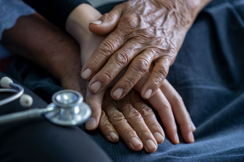 A close-up of a young nurse holding the wrinkled hands of an older person.