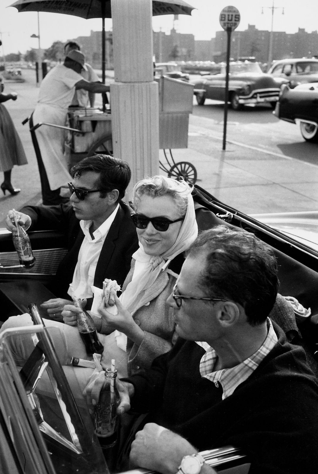 Marilyn Monroe and playwright Arthur Miller in a convertible car eat a hot dog