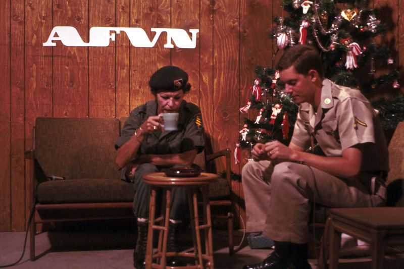 Martha Raye being interviewed by Dick Ellis. Raye and Ellis sit on chairs next to a decorated Christmas tree in a wood-paneled room.