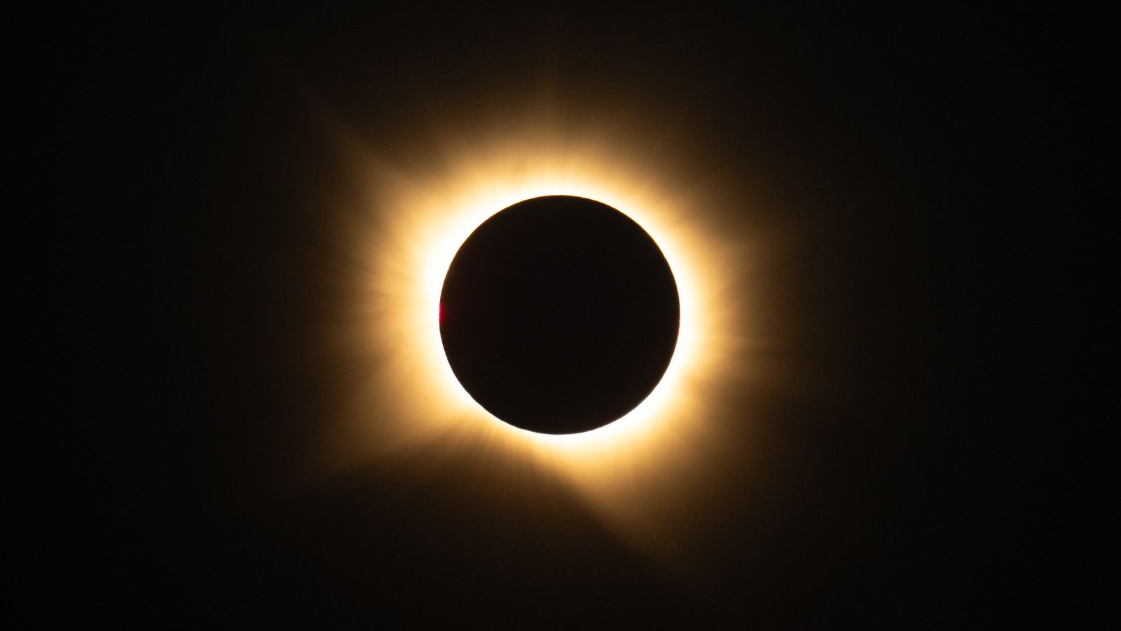 The sun's corona glowing around the dark disk of the moon during totality over a Spanish landscape.