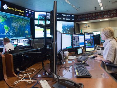 For three years, Lauren Cooper has been an ISS operations engineer. In the Johnson Space Center mission control room, she remains alert (note coffee cup) through eight-hour shifts.