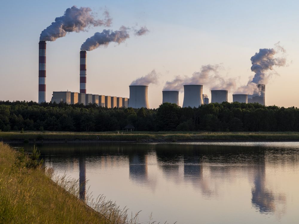 A coal power plant releasing smoke in front of a body of water