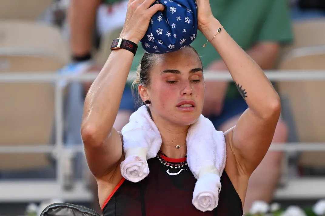 a tennis player puts a cloth bag with snowflakes on her head and has a cold towel around her neck
