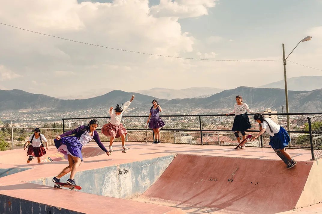 A group of women skating at a skatepark, mountains in the background.