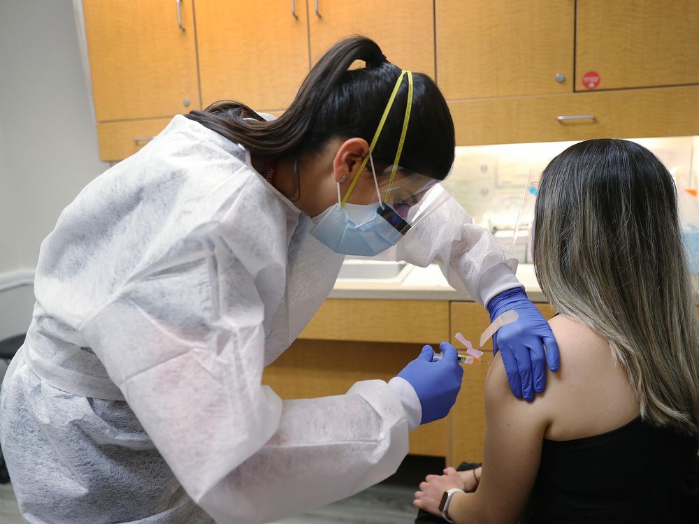 A nurse practitioner wears personal protection equipment as she administers a flu vaccination to a patient