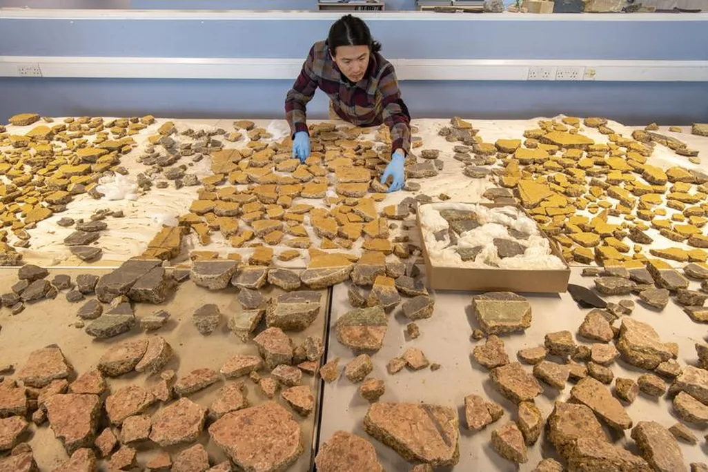 A man bending over a table full of fragments from frescoes