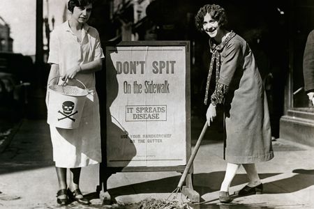 Allene Goodenough (right) and Helyn James of the Young Women's Christian Association mop up a spot on the sidewalk where someone expectorated by an anti-spitting sign during a public health campaign in Syracuse, New York, in 1900. 