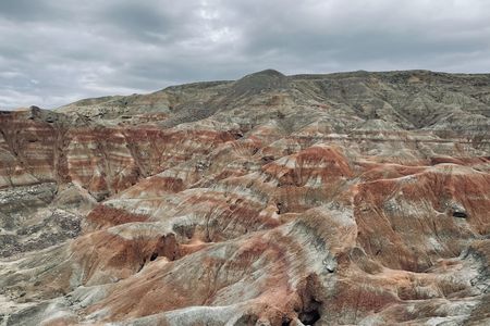 A grey, orange, and brown expanse of layered rock formations under a gray sky.