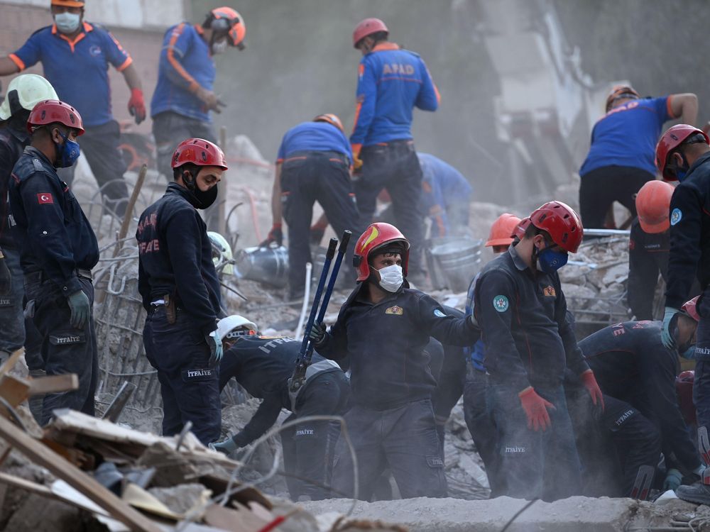 Search and rescue workers in red helmets look through debris for survivors of the October 30 earthquake