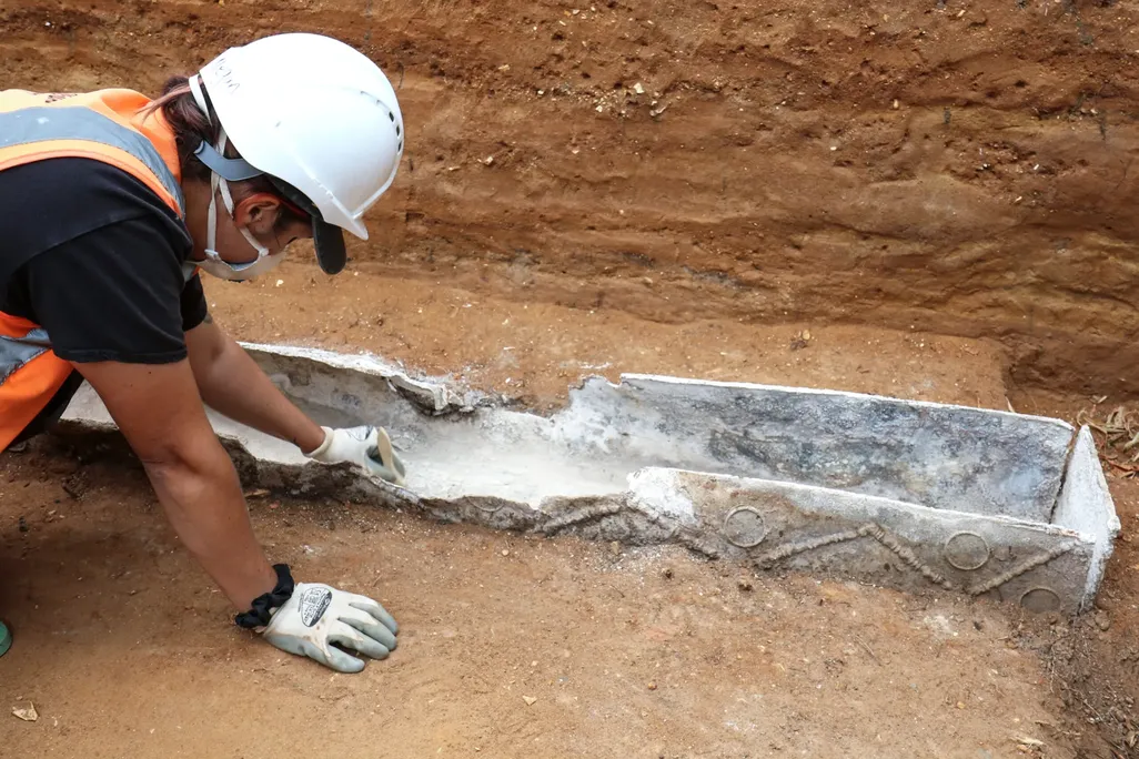 A person wearing an orange vest excavating a coffin