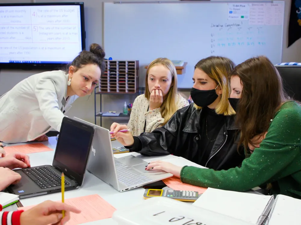 Peterson wears a bun and blazer pointing towards a computer screen with her students