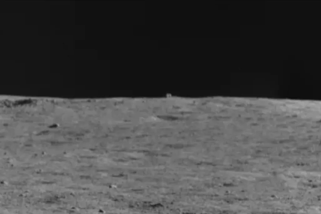 A black and white images of the lunar surface with a small cube-shaped object on the horizon