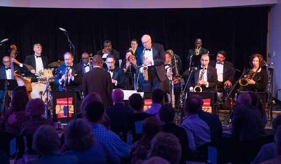 A group of jazz musicians perform on a stage to a live audience