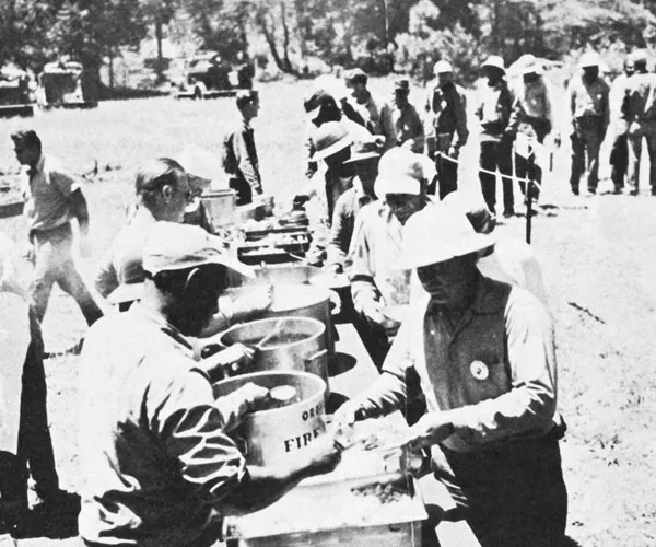 Prisoners and staff waiting in line for food at a field kitchen