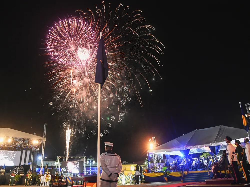 Fireworks illuminate the night sky behind a Barbadian national flag