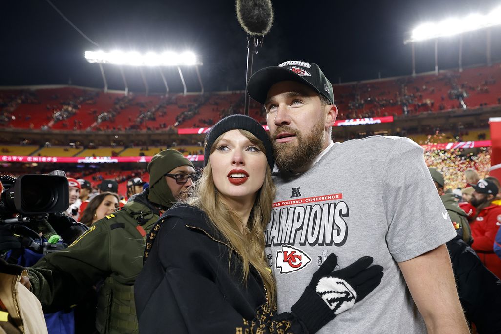A woman with blonde hair and a black hat next to a football player
