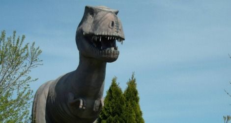 A Tyrannosaurus stands over the remains of an abandoned mini-golf course.