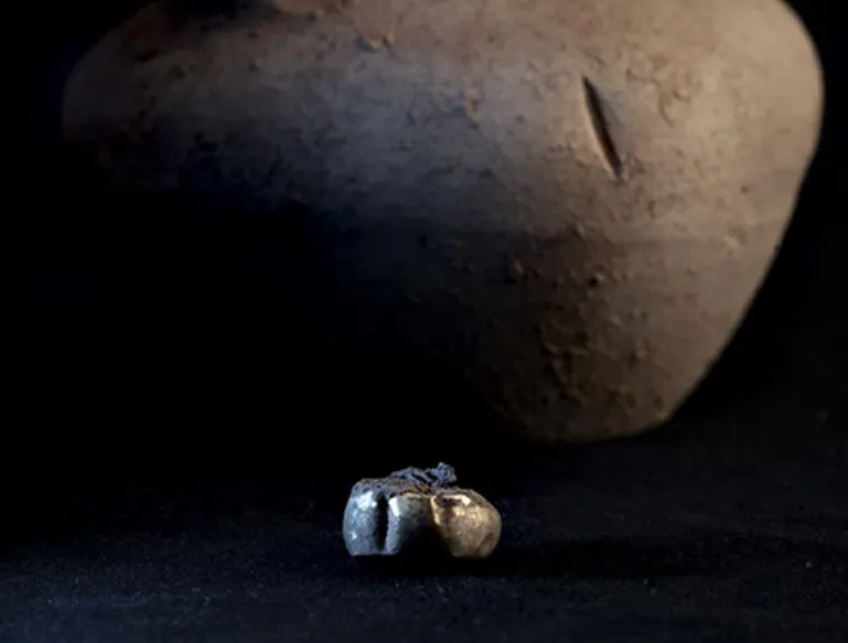 A golden earring sits in front of the brown pot it was discovered within.