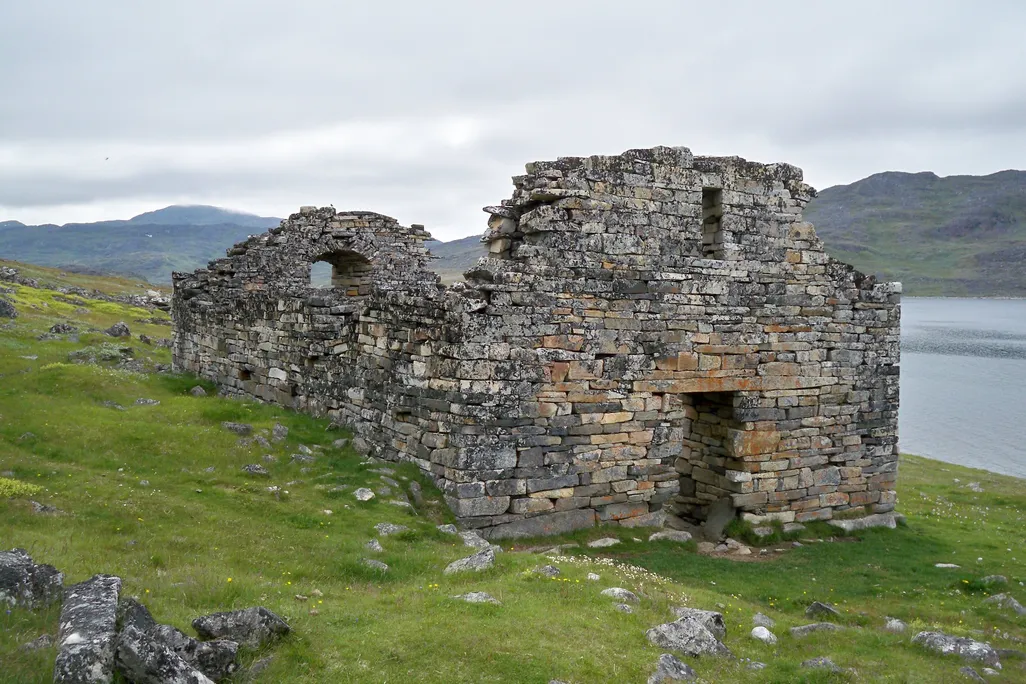 ruins of a gray and brown stone building on green landscape overlooking lake
