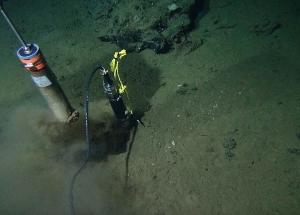 A murky green-brown ocean floor with a tool drilling into the seafloor