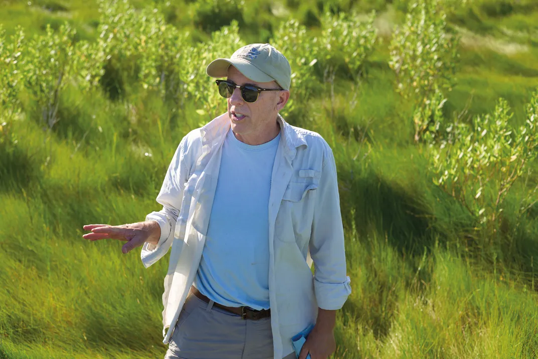 a man with a ball cap and sun glasses stands in a salt marsh