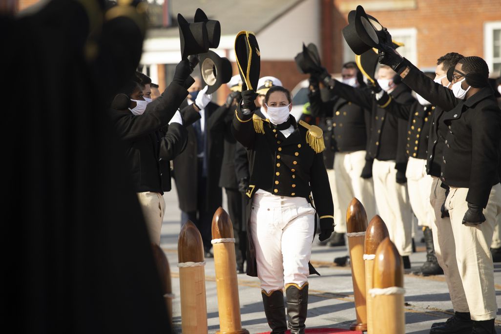 woman in black navy dress uniform being saluted by two rows of fellow sailors