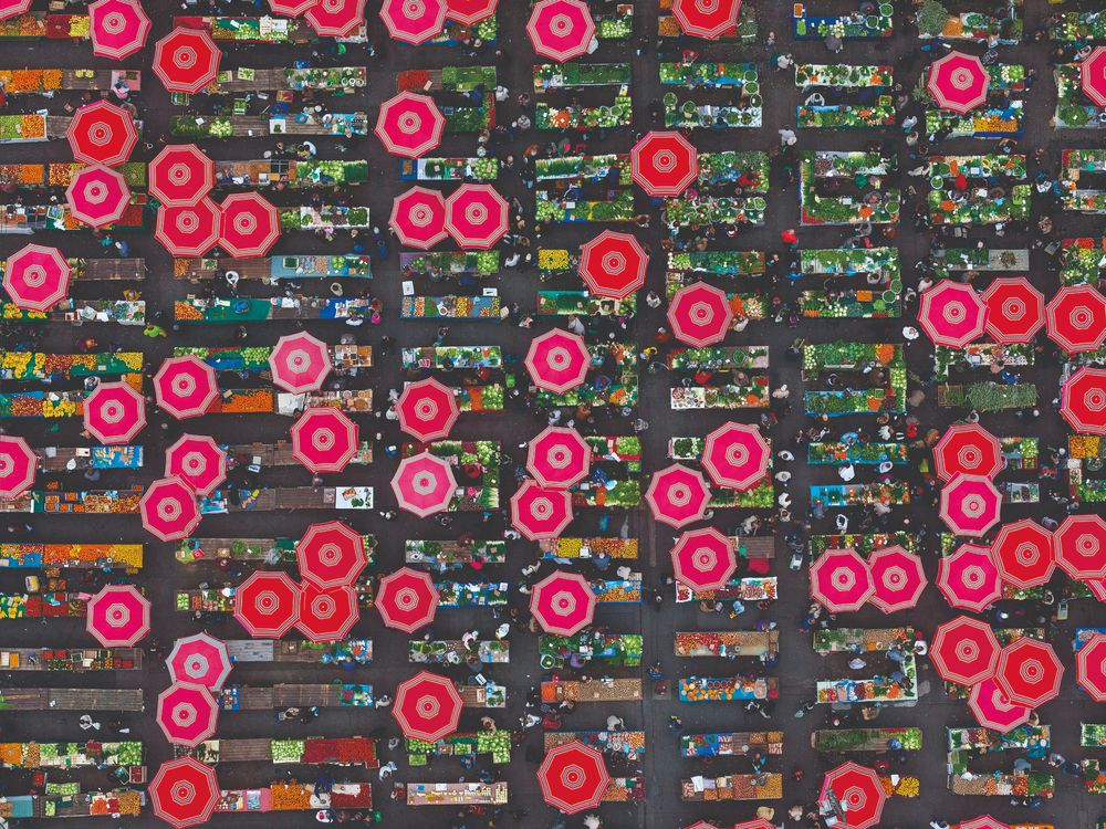 Aerial view of Zagreb’s Dolac Market, with rows of produce stalls and dozens of bright red umbrellas forming a colorful pattern across the busy open-air marketplace.