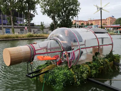 Performance artist Abraham Poincheval stands inside a giant glass bottle on the Canal Saint-Denis.