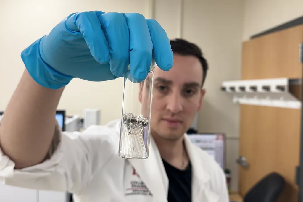 Researcher wearing a lab coat holding up a vial of samples