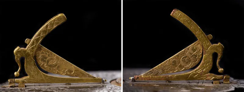 A pocket sundial's golden gnomon, seen from two angles. The gnomon's support has been shaped to look like a crouched bird, with the beak of the bird adjusted to point to the latitude of the observer.