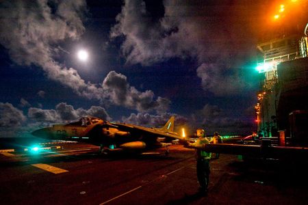 U.S. Navy flight deck personnel taxi an AV-8B Harrier assigned to Marine Attack Squadron 542 across the flight deck aboard the amphibious assault ship USS Bonhomme Richard in 2012. Should amphibious assault ships replace the traditional aircraft carrier?
