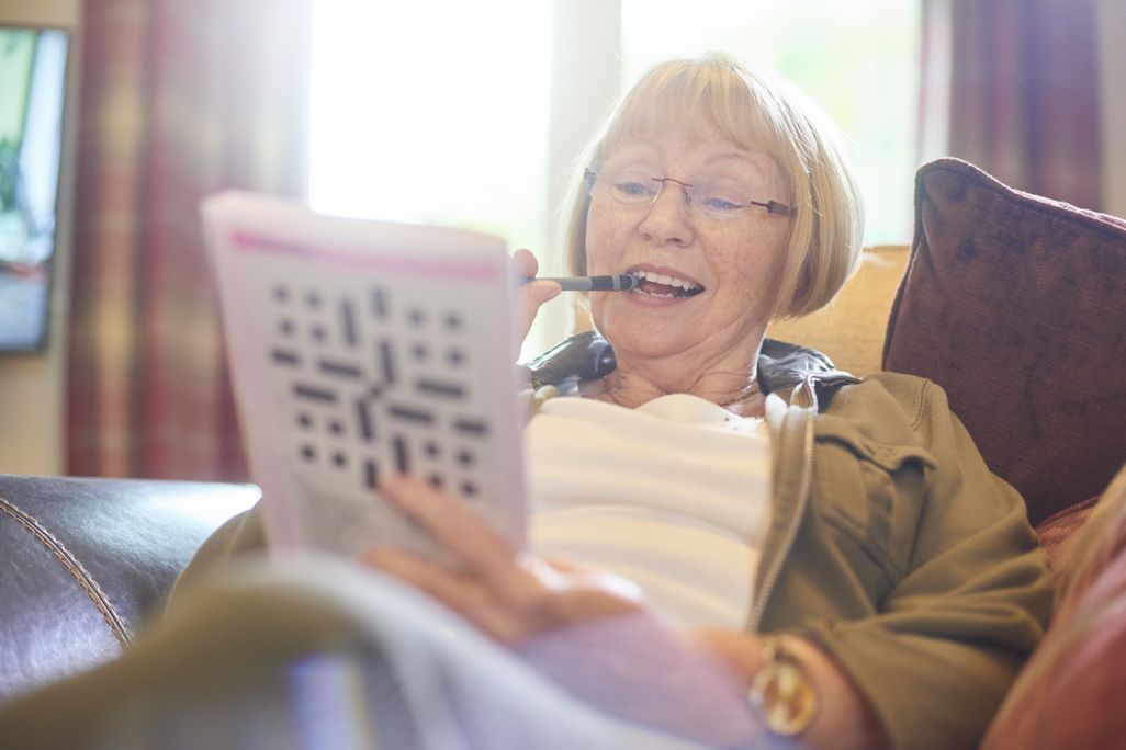 An elderly woman smiles as she does a crossword puzzle