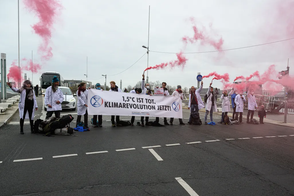 Protesters in Berlin wear white lab coats and hold a sign