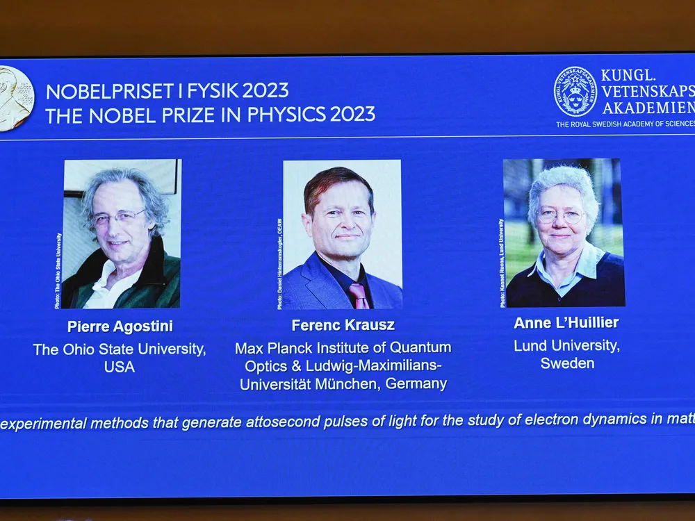 An image on a projector screen with photos of the three recipients of the 2023 Nobel Prize in Physics