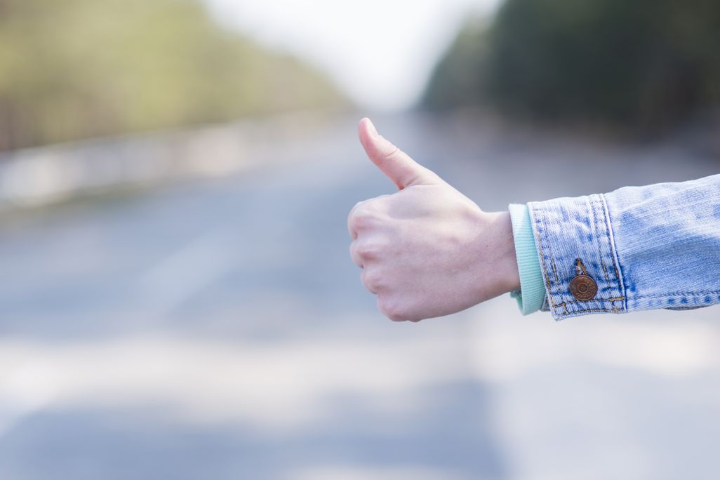 one human hand in a thumbs up position with a road blurry in the background