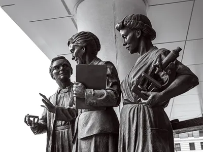 <p>This seven-foot statue of Pearl Kendrick, center, and Grace Eldering, left, was unveiled in Grand Rapids in 2019. Lab assistant Loney Clinton stands to the right with a microscope.</p>