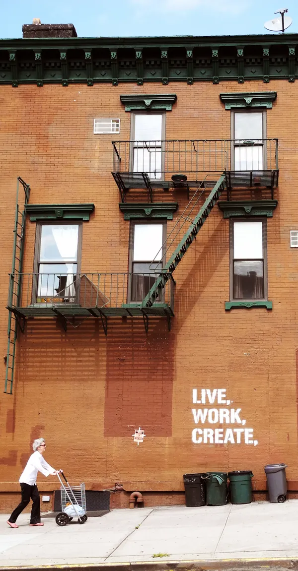 Elderly lady walking up the hill on Park Slope, Brooklyn, NY. Wall graffiti reads "LIVE, WORK, CREATE." thumbnail